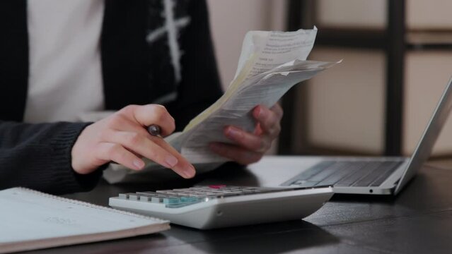 Woman checking bills, taxes, bank account balance and calculating expenses in the living room at home or office. Close up