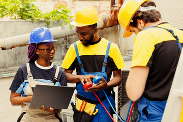 Happy knowleadgeable engineers checking refrigerant levels in condenser while using manometers to...