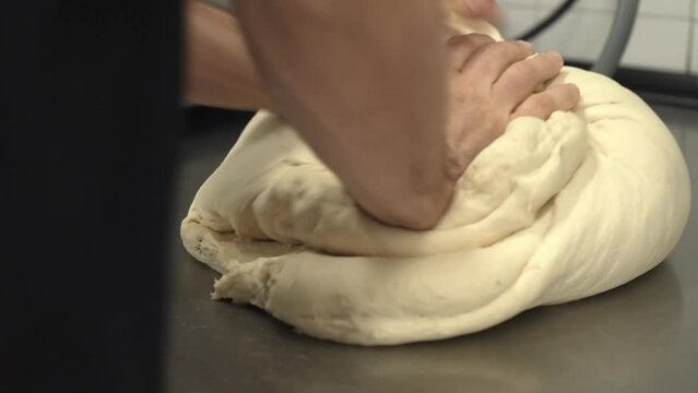 baker manually kneading raw bread dough on a table (2)