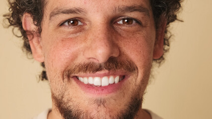 Close-up portrait of guy with curly hair and freckles looking at the camera with smile in studio on beige background