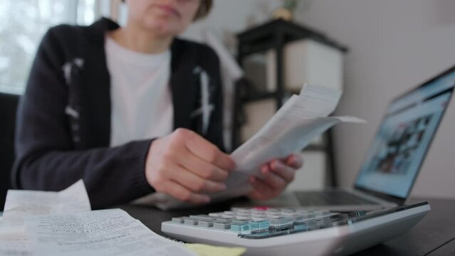 Woman checking bills, taxes, bank account balance and calculating expenses in the living room at home or office. Close up footage