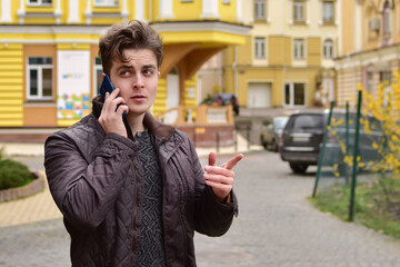 An attractive man with curly hair in an autumn jacket speaks on the phone on the street.