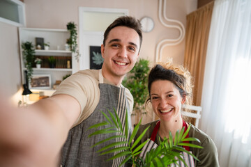 Couple caucasian man and woman wife and husband planting flowers together taking care of home plants real people domestic life family gardening concept take selfie photo with smartphone UGC