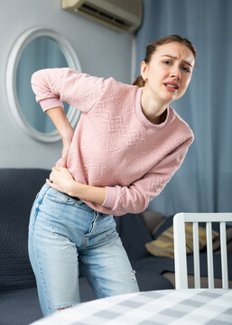 Portrait of young adult woman with hands on waist suffering from back pain at home