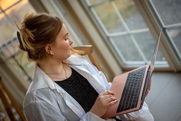 concept: online education. A young girl in a home environment with a computer in her hands, with a smile, dressed in a white shirt, top vie