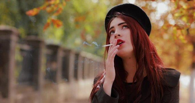 Young woman smoking cigarette at the autumn park, slow motion