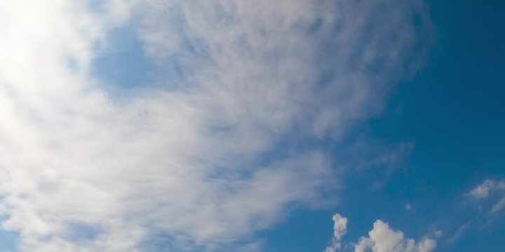 Blue sky with light feather clouds spreading above. Sun lights the small clouds floating by the horizon. Low angle view. Timelapse.