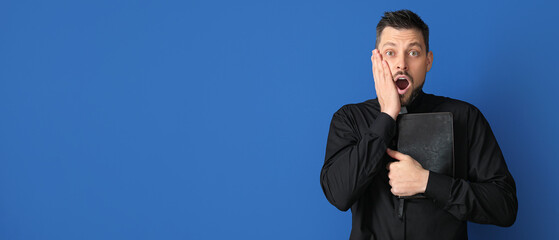 Surprised priest holding Bible on orange background with space for text
