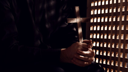 Young priest with cross in confession booth - obrazy, fototapety, plakaty