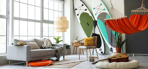 Stylish interior of room with sup boards, hammock and sofa