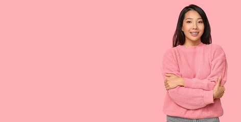 Fototapeta premium Young Asian woman hugging herself on pink background with space for text