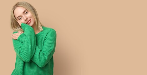 Young woman hugging herself on beige background with space for text