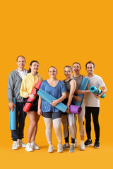 Group of sporty young people with fitness mats on yellow background