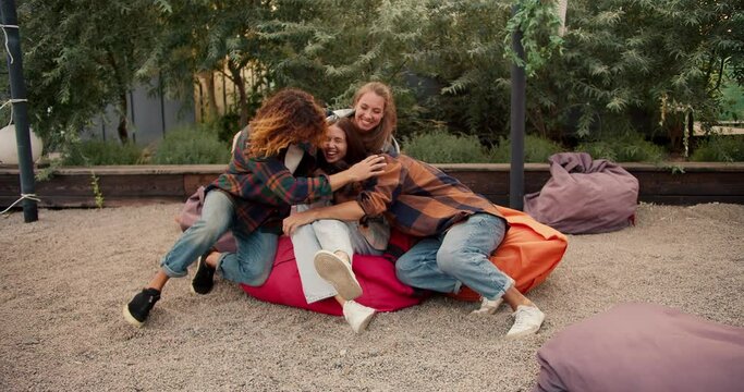 A brunette girl sits on a bean bag chair. Three friends run up to the girl and hug her. Rest in the country house