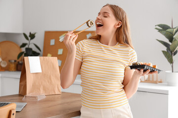Happy young woman eating sushi in kitchen