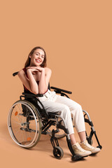 Young woman in wheelchair on beige background