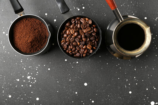 Cezve and measuring cups with ground coffee and beans on black grunge background