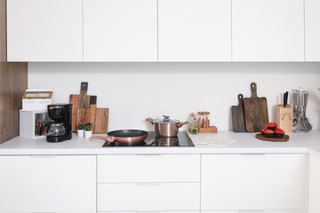White kitchen countertop with electric stove, frying pan, cooking pot and utensils