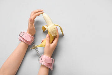 Woman with pink handcuffs and fresh banana on light background. Sex education concept