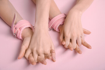 Women with handcuffs from sex shop on pink background, closeup. Sex education concept