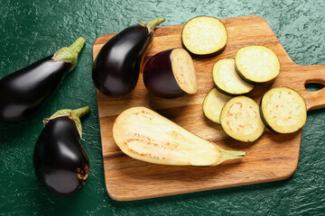Wooden board with fresh eggplants on green background