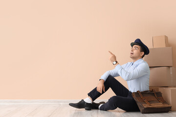 Fototapeta premium Young male postman in uniform pointing upward with hand gesture, delivery service and mail carrier occupation