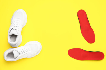 Pair of stylish sneakers and orthopedic insoles on yellow background