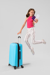 Little girl with passport, ticket and suitcase jumping on grey background