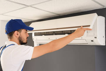 Male technician fixing air conditioner in room