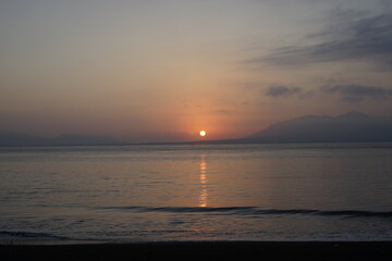 Sunrise or sunset view with a small looking sun in the distance on a beach.