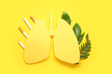 Paper lungs with cigarettes and green leaves on yellow background. Lung cancer concept