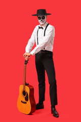Young man with painted skull and guitar on red background. Mexico's Day of the Dead (El Dia de Muertos) celebration