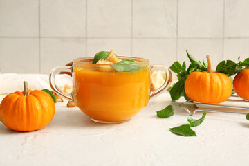 Glass pot of delicious pumpkin cream soup with basil and croutons on white table