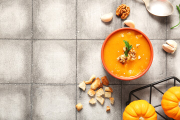 Bowl of delicious pumpkin cream soup with walnut, parsley and croutons on grey tile background