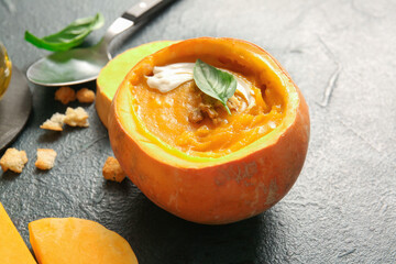 Delicious cream soup with walnut and basil in pumpkin on dark background