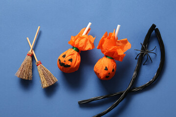 Sweet lollipops with liquorice and brooms for Halloween party on blue background