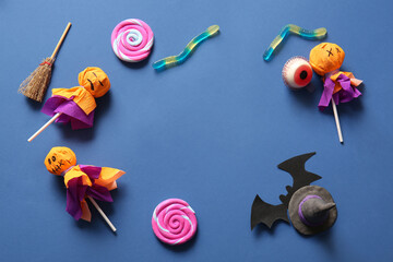 Frame made of sweet lollipops with witch hat, jelly worms and eye for Halloween party on blue...