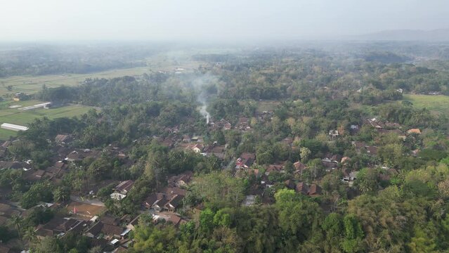 Aerial view of human settlement buildings expansion near paddy rice fields in the morning sunlight. Kulon Progo rural village landscape. Population density is displacing agricultural land and forests.