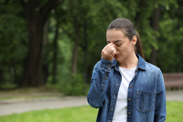 Woman suffering from seasonal spring allergy in park, space for text