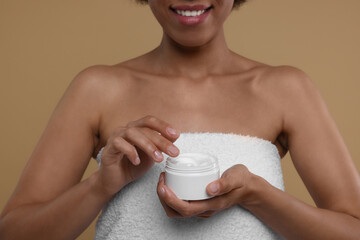 Young woman holding body cream on beige background, closeup