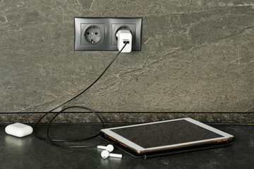 Tablet charging from electric socket on dark grey table indoors