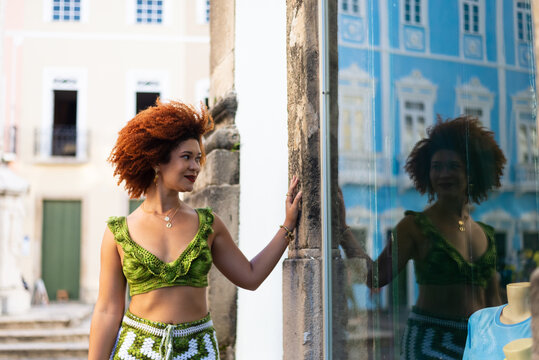 Beautiful woman with red hair standing next to a glass door that reflects her image.