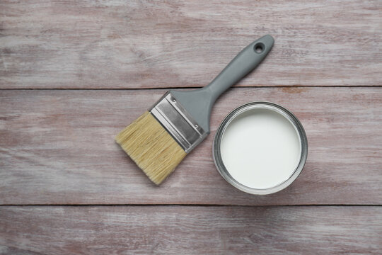 Can of white paint and brush on wooden table, flat lay