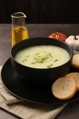 Bowl of tasty leek soup and bread on grey table, closeup