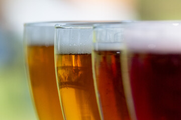 Small curved tulip shaped sample glasses of pale ale beer with froth on the top. The liquid alcohol has a vibrant yellow tint. The glasses are on a wooden table with circles.