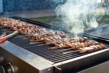 Multiple pieces of chicken skewers and pork kebabs grilling on a barbecue grill. There's smoke...