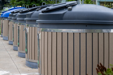 A row of industrial round compost bins. The containers are black plastic on top and wooden on the...