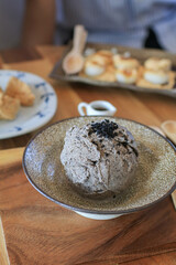 Homemade Black sesame ice cream with spoon in ceramic bowl on wooden table. Copy space. Trendy summer food