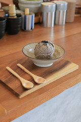 Homemade Black sesame ice cream with spoon in ceramic bowl on wooden table. Copy space. Trendy...