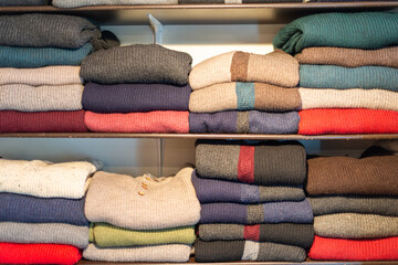 Multiple shelves of colorful natural wool, mohair, and cashmere knitted sweaters are on display.  The folded and stacked casual apparel are both cardigan and pullover styles for sale in a retail shop. - obrazy, fototapety, plakaty